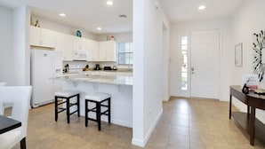 A modern kitchen with white cabinets, a central island, and two bar stools. - Grand Superior 4BD Pool Home at Disney Universal (Davenport)