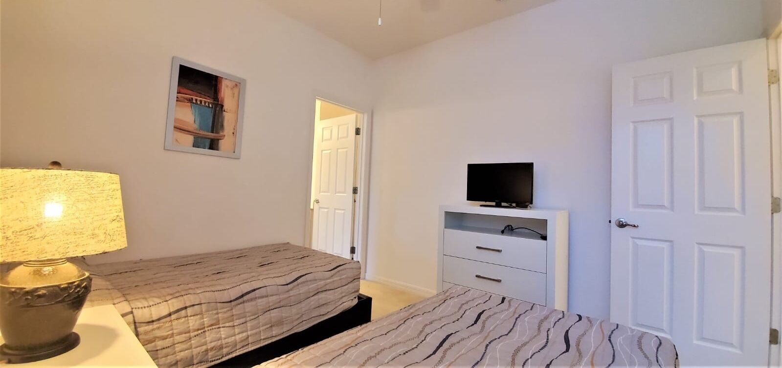 A bedroom with a bed, a bedside lamp, a TV on a stand, and a door.