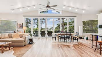 A spacious living area with a large sliding glass door leading to an outdoor deck, a ceiling fan, and a dining table with chairs.