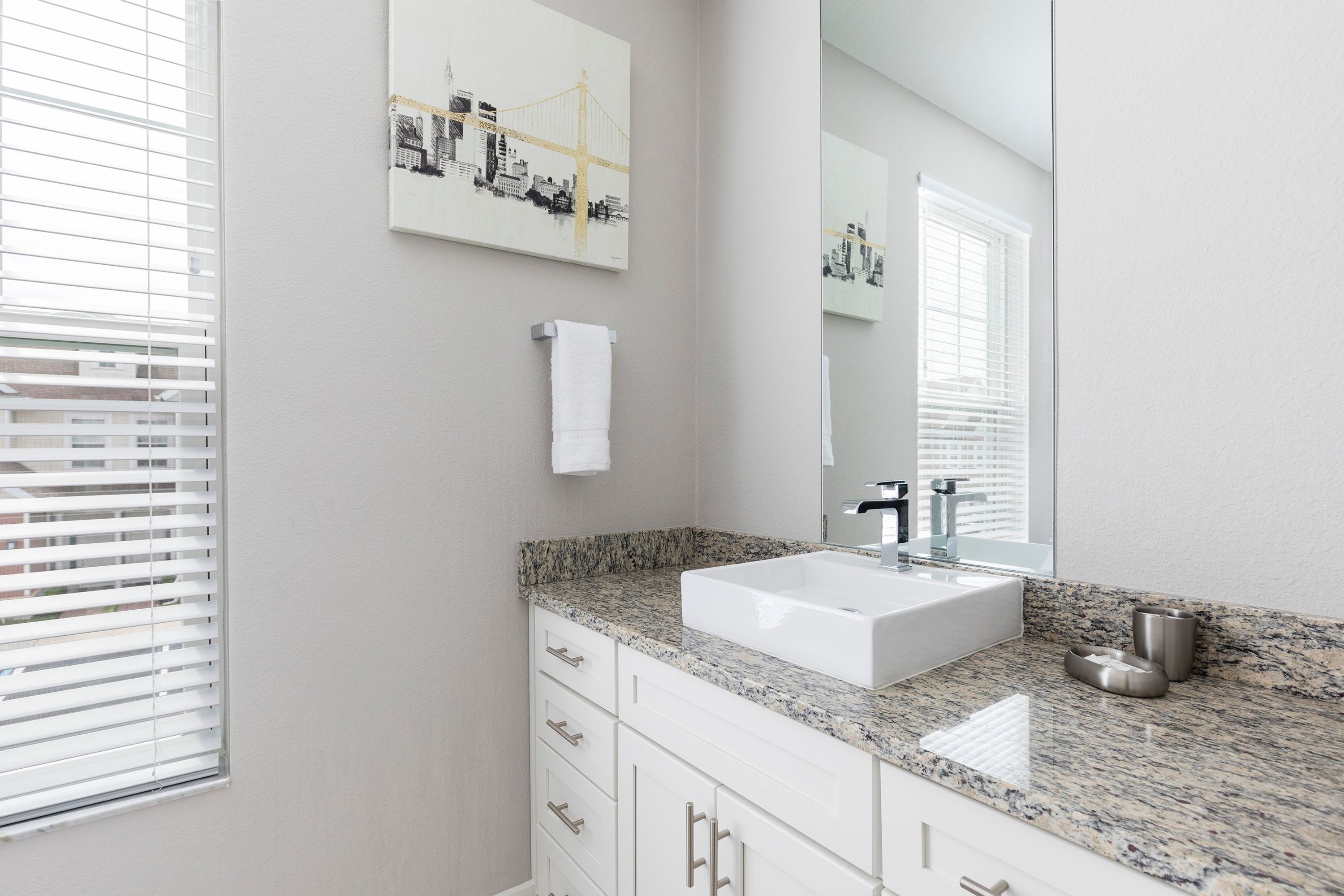 A modern bathroom with a white sink, granite countertop, and a large mirror.