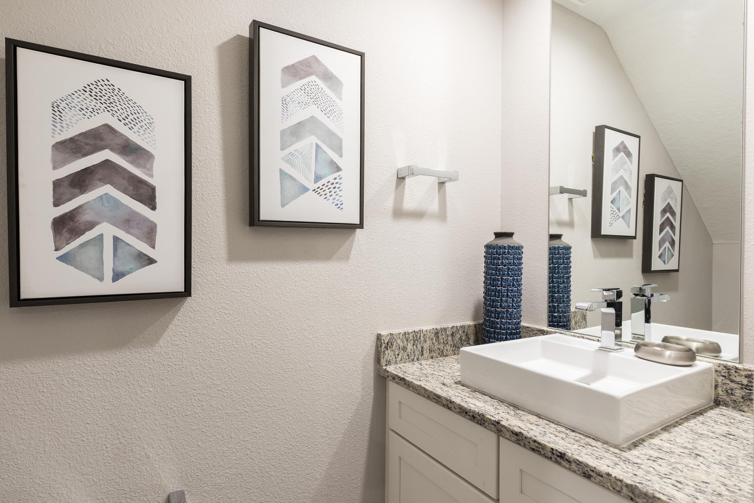 A bathroom with a white sink, framed artwork on the wall, and a mirror above the sink.