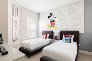 A bedroom with two beds, a desk, and a Mickey Mouse mural.