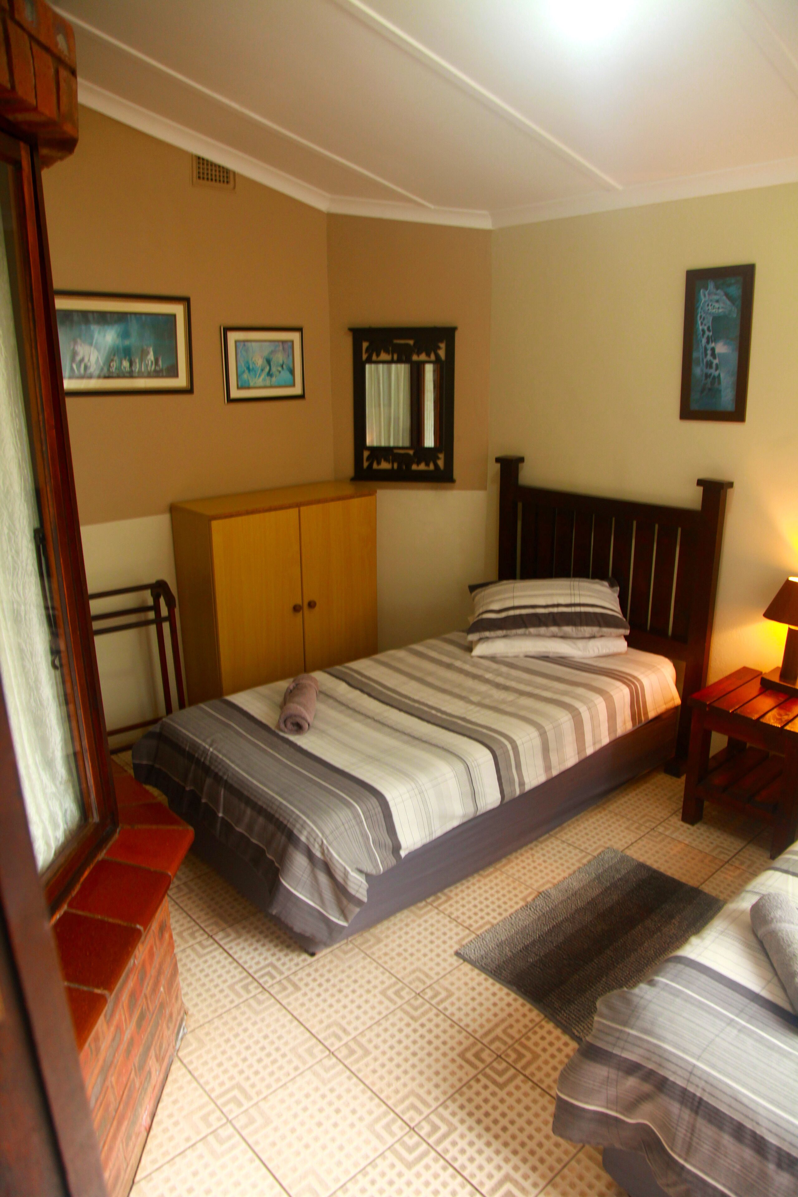 A bedroom with a bed, wooden wardrobe, and a nightstand with a lamp.
