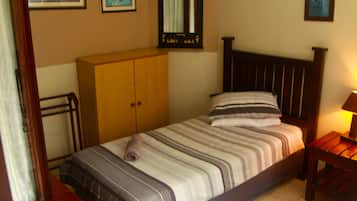 A bedroom with a bed, wooden wardrobe, and a nightstand with a lamp.