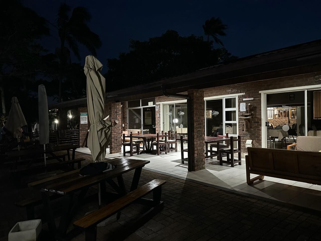 An outdoor patio area with brick flooring, wooden tables, and benches.