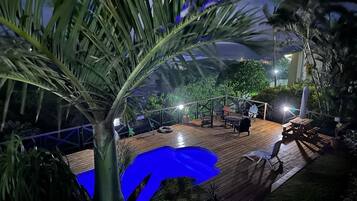 Um deck de madeira com piscina, cercado por palmeiras e plantas em vasos.
