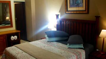 Habitació d'hotel amb un llit, taules de nit, una taula auxiliar, una làmpada, un quadre amb marc a la paret i una porta.