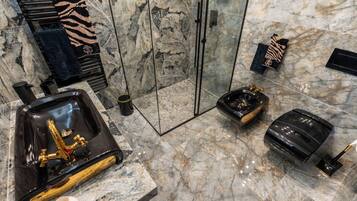 A bathroom with a marble floor, a black bathtub, a gold faucet, and towels on a rack.