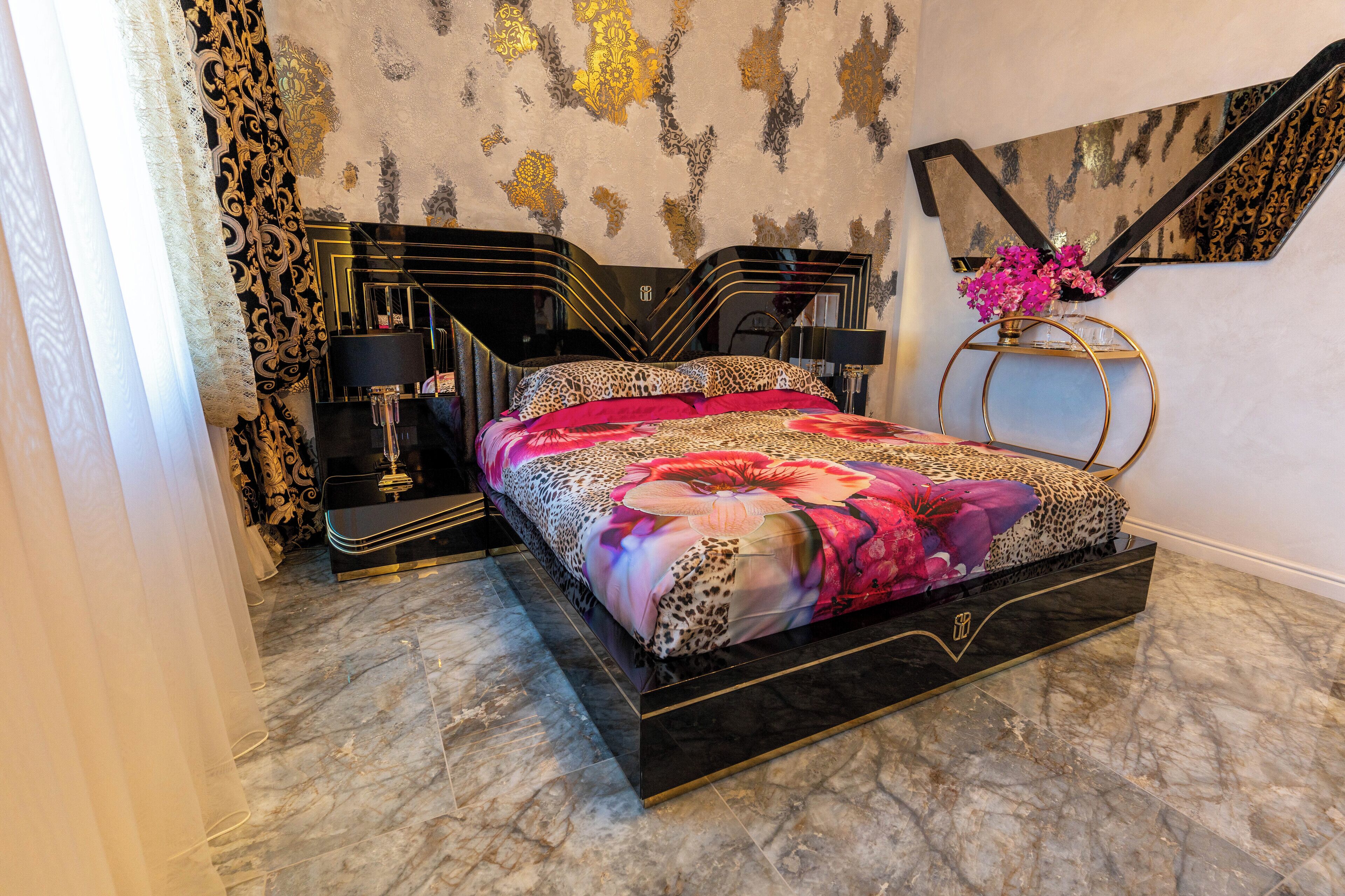 Une chambre à coucher avec un lit noir et doré, un sol en marbre et un mur décoratif agrémenté de motifs dorés.