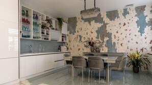 A modern kitchen with white cabinets, a marble countertop, and a dining area with a table and chairs. - Luxury Suites (Cluj-Napoca)