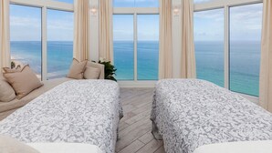 Una habitación con dos camas, un sofá y un ventanal con vistas al mar.