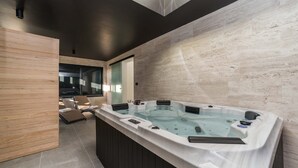 A modern bathroom with a freestanding jacuzzi, wooden paneling, and a glass door leading to a seating area. - Villa Antea Dalmacija (Privlaka)