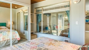 A bedroom with a wooden ceiling, a large bed with a colorful quilt, a window with curtains, and a view of the outside. - Stardust Dunes Condo (Ocean Shores)