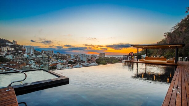 An infinity pool with a city view at sunset. - Casa Costera | Walk to Romantic Zone & Beach (Puerto Vallarta)