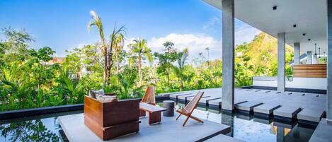 Zona de piscina exterior con mobiliario moderno y vistas a exuberante vegetación.