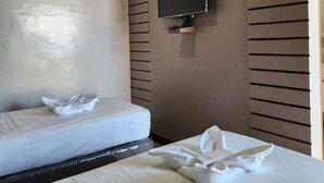 Une chambre d’hôtel avec deux lits, un téléviseur à écran plat fixé au mur et un motif décoratif en lattes de bois sur le mur.