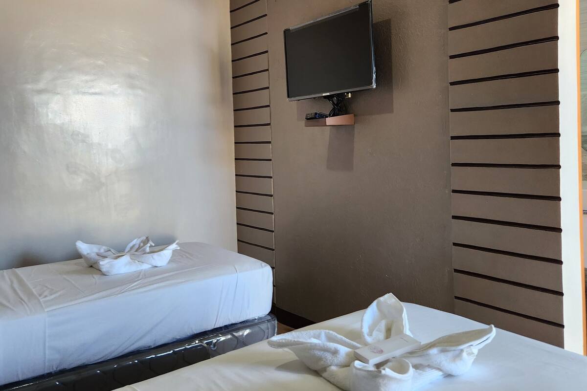 Ein Hotelzimmer mit zwei Betten, einem an der Wand befestigten Flachbildfernseher und einer Wandgestaltung aus Holzlamellen.