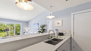 Een moderne keuken met een groot eiland, witte marmeren aanrechtbladen en uitzicht op weelderige begroeiing.