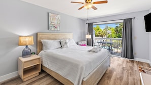 Een moderne slaapkamer met een bed, nachtkastje, plafondventilator en een balkon met een tafel en stoelen.
