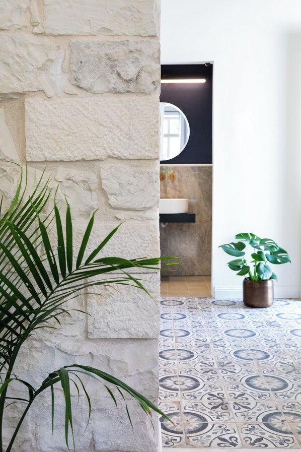 A room with a stone wall, a patterned floor, a sink, and a potted plant. - Mila Boutique Hotel (Haifa)