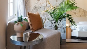 A cozy room with a stone wall, a round mirror, a sofa with cushions, a small round table, and a potted plant. - Mila Boutique Hotel (Haifa)
