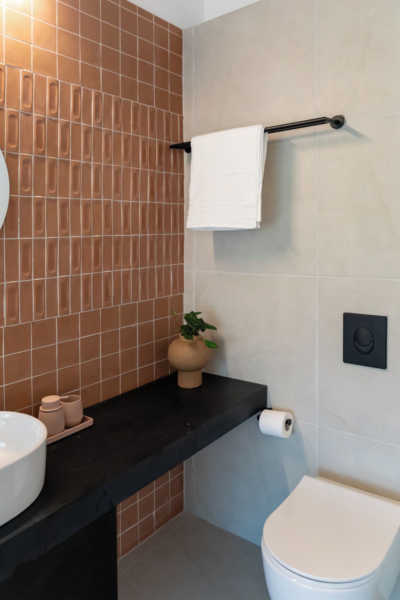 Un baño con encimera negra, lavabo blanco, inodoro y toallero.