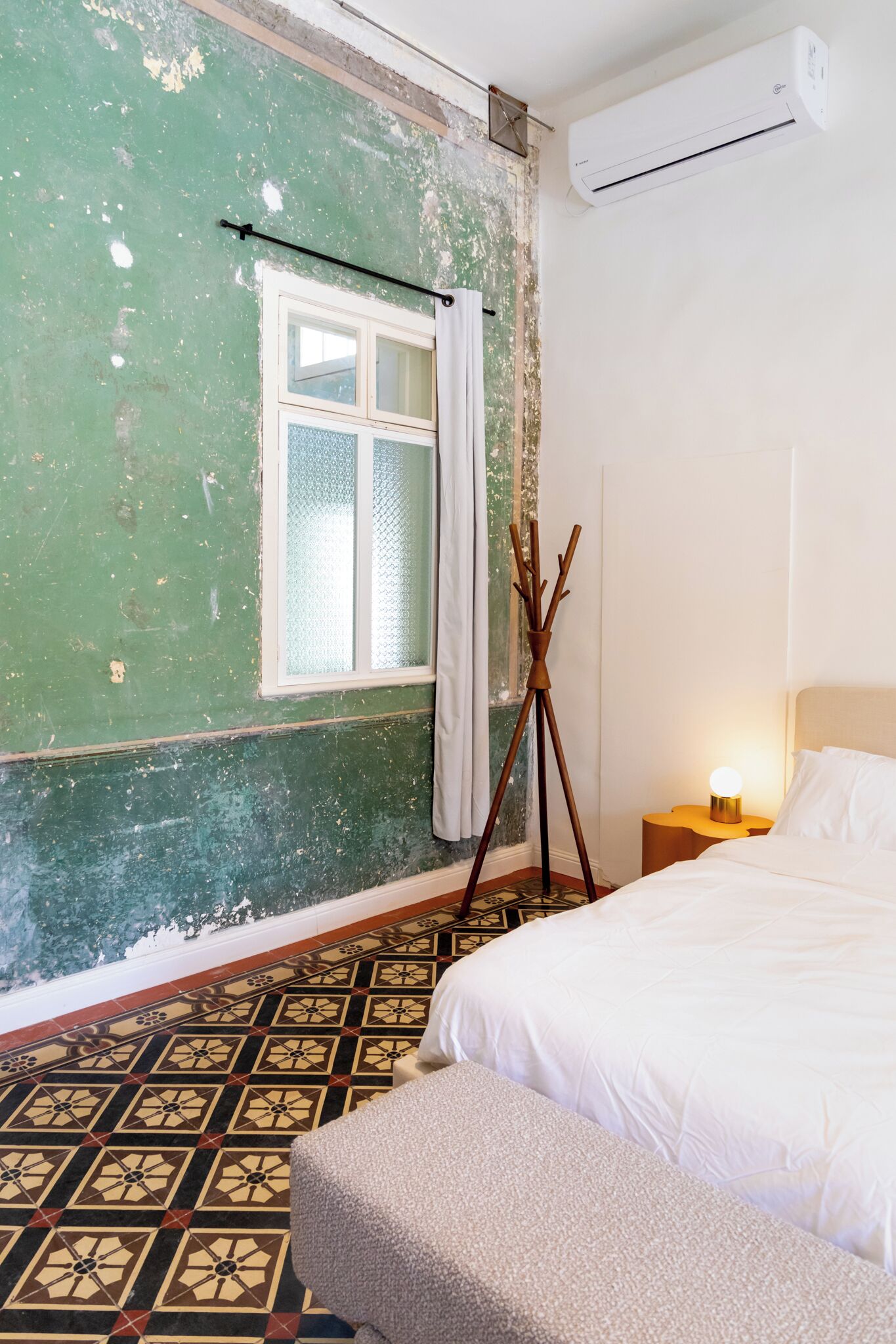 A room with a bed, a tripod lamp, a window with curtains, and an air conditioner.
