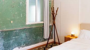 A room with a bed, a tripod lamp, a window with curtains, and an air conditioner.