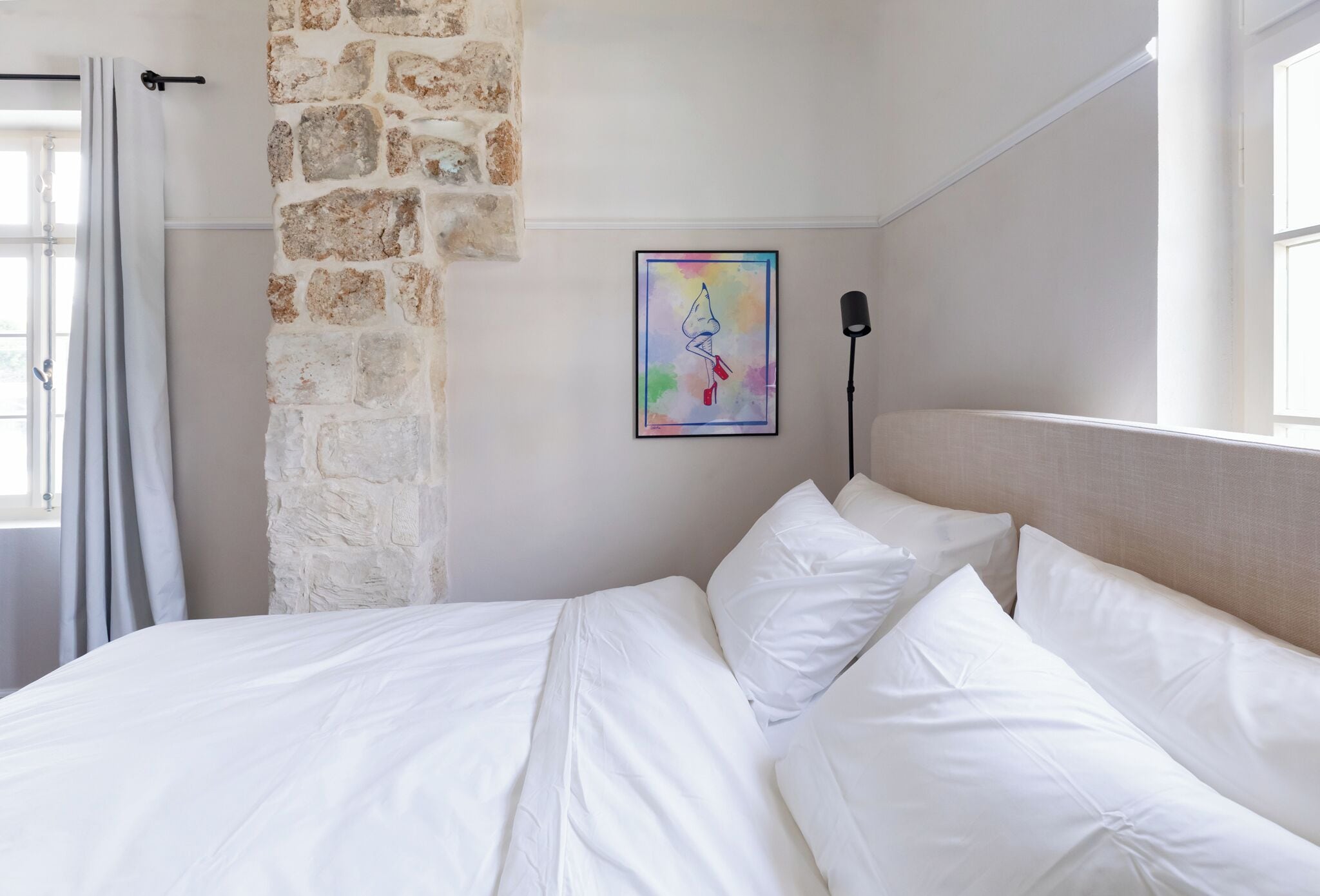 Un letto rifatto con lenzuola bianche, un muro in pietra e un'opera d'arte colorata appesa al muro.