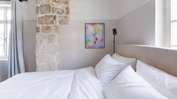 Un letto rifatto con lenzuola bianche, un muro in pietra e un'opera d'arte colorata appesa al muro.