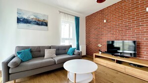 Un salon moderne avec un canapé gris, une table basse blanche et un téléviseur à écran plat fixé à un mur en briques.