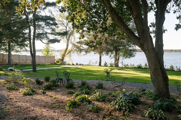 A landscaped garden with a lawn, trees, and a body of water in the background. - Lakecroft (Prince Edward)
