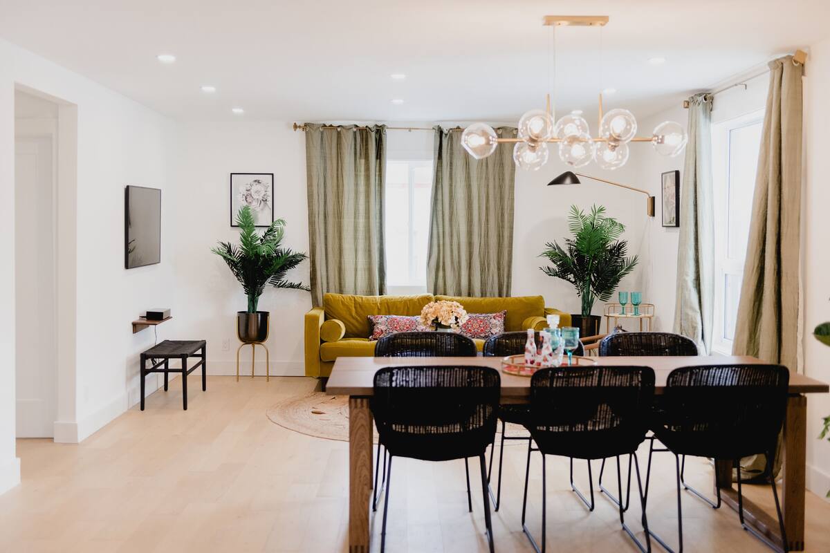 Un comedor con una mesa de madera, sillas negras, un sofá amarillo y cortinas verdes.