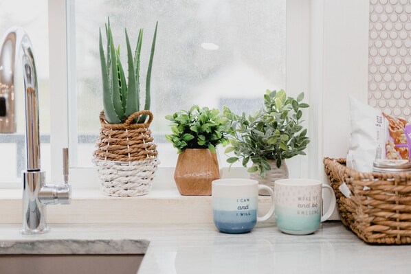 A kitchen counter with a sink, two potted plants, and two mugs with motivational phrases. - Lakecroft (Prince Edward)