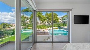 A modern bedroom with a large sliding glass door leading to a pool area. - Large private estate 700 feet from the beach featuring a 36 sqm heated private pool, 5 cozy en suite bedrooms, seven bathrooms, and 3 separate kitchen areas (Podstrana)