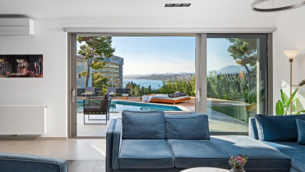 A modern living room with a blue sofa, a coffee table, and a view of a pool and outdoor seating area. - Large private estate 700 feet from the beach featuring a 36 sqm heated private pool, 5 cozy en suite bedrooms, seven bathrooms, and 3 separate kitchen areas (Podstrana)