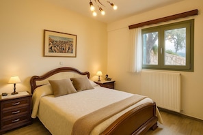 A bedroom with a bed, two bedside tables, a lamp, a framed picture on the wall, a window with a view, and a radiator.