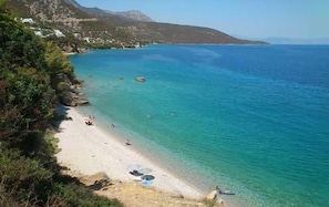 A beach with clear turquoise water, a sandy shore, and a few people swimming.