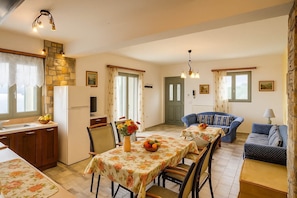 A cozy living room with a sofa, a dining table with chairs, a kitchen area with a refrigerator, and a stone wall.