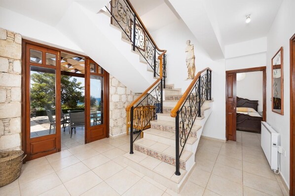 Un intérieur spacieux avec un escalier menant à un balcon, des murs en pierre et une vue sur l’extérieur.