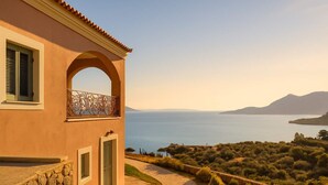 A Mediterranean-style building with a stone pathway leading to a balcony overlooking a body of water and hills. - Filistron Seaview Bliss - Coastal Charm Hideaway (Taktikoupoli)