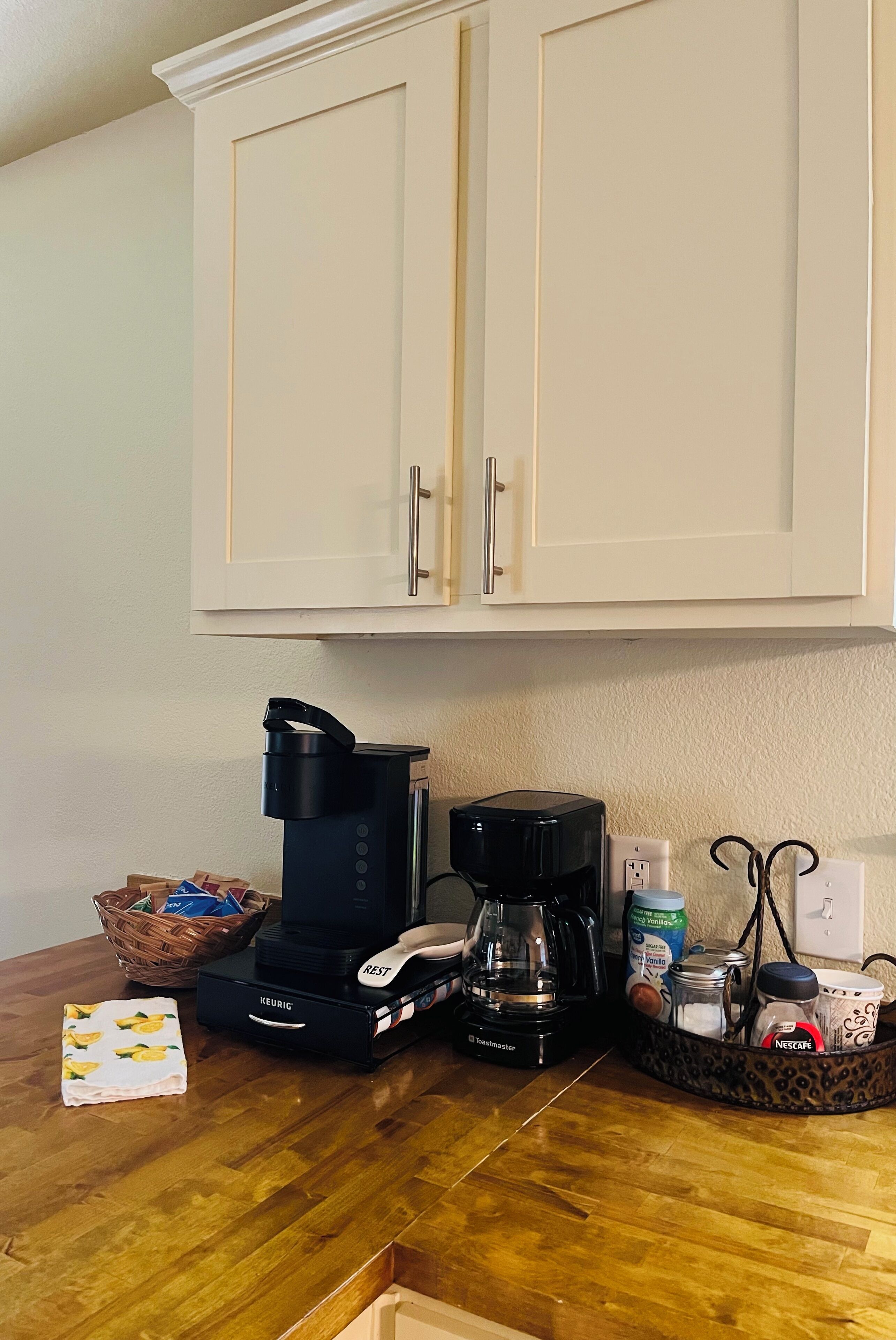 Eine Küche mit Kaffeemaschine, Wasserkocher und einer Korb voller Gegenstände auf der Arbeitsfläche.