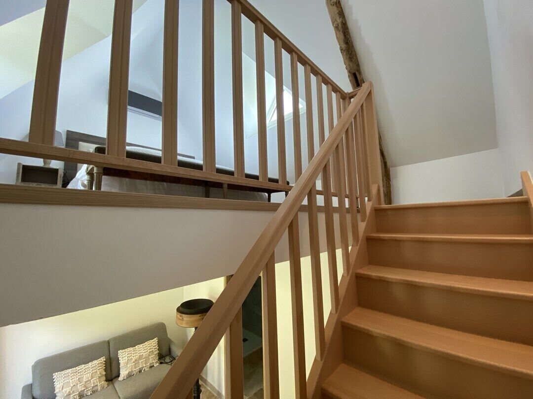 Una escalera de madera con vista a una sala de estar inferior, que incluye un sofá y una lámpara.