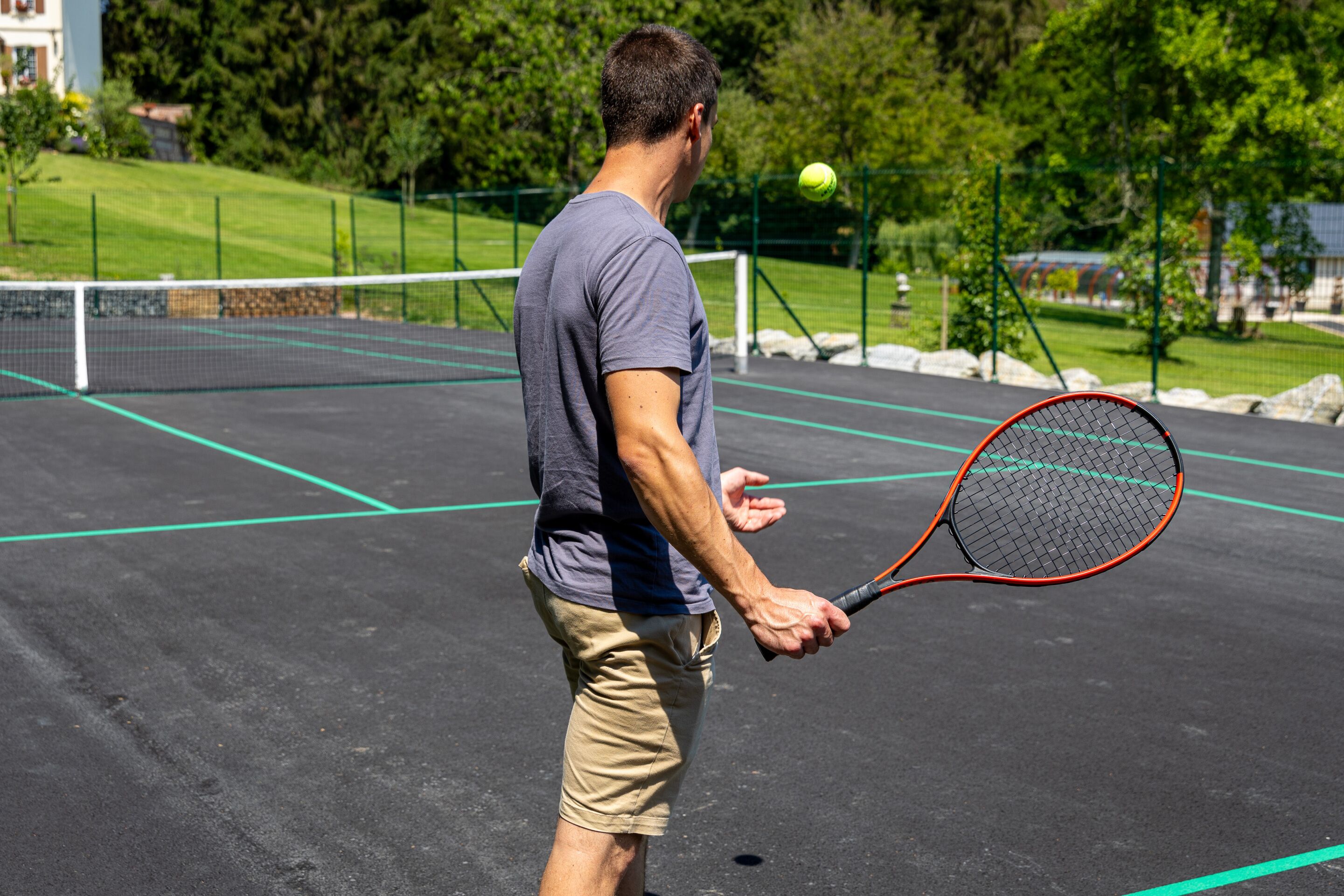 A tennis court with a net, a tennis ball in mid-air, and a player holding a racket.