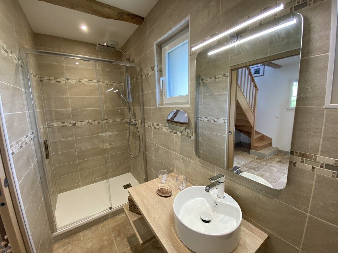 Un baño con ducha acristalada, un lavabo con espejo y una ventana que proporciona luz natural.