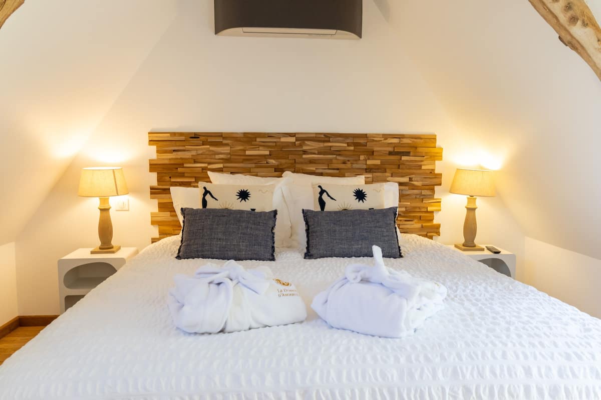A neatly made bed with a wooden headboard, two bedside lamps, and two towels on the bed.