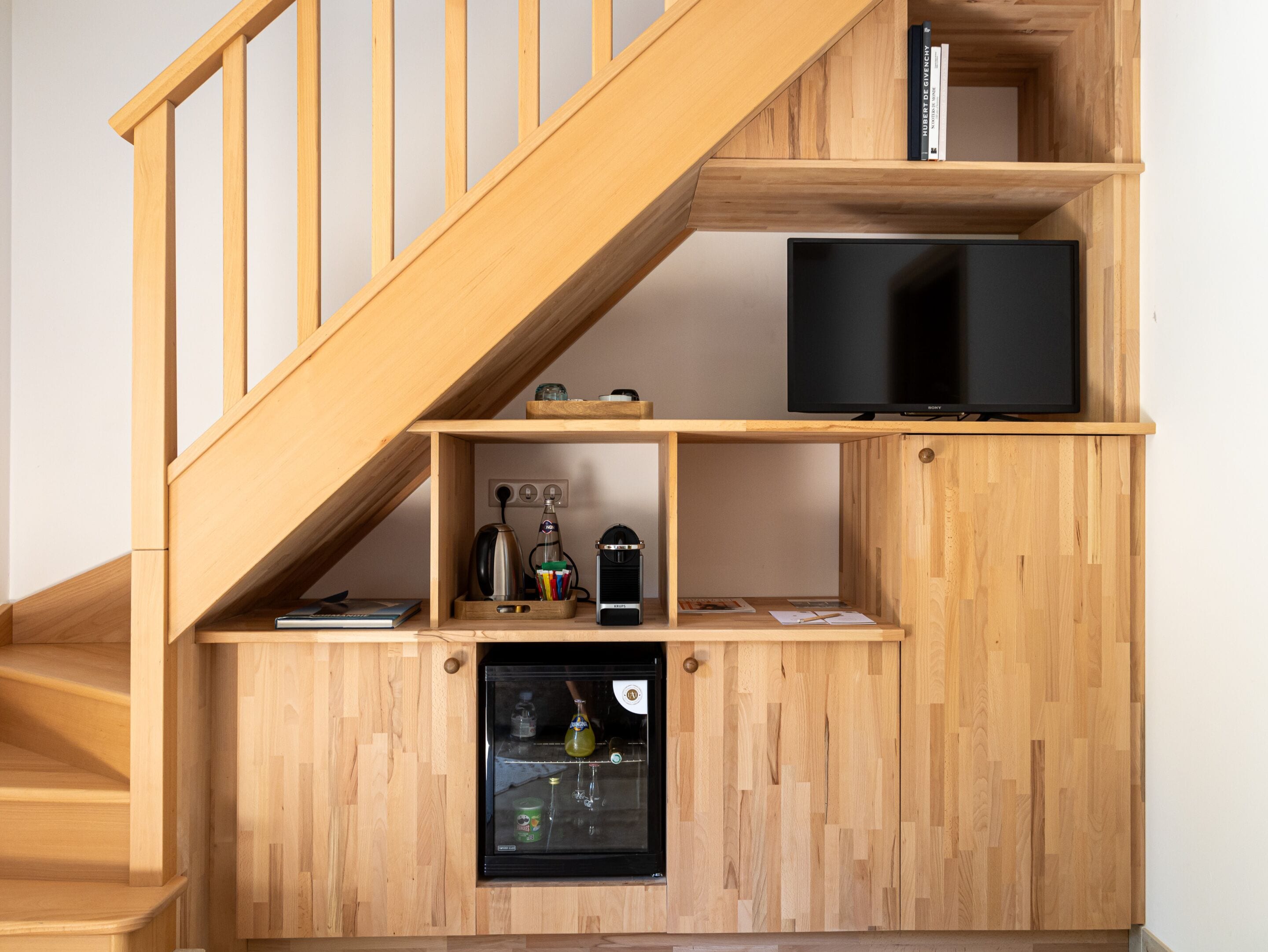 A multi-level wooden interior with a staircase, a television, a mini-fridge, and shelves with various items.