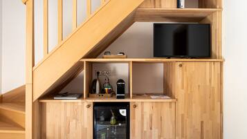 A multi-level wooden interior with a staircase, a television, a mini-fridge, and shelves with various items.