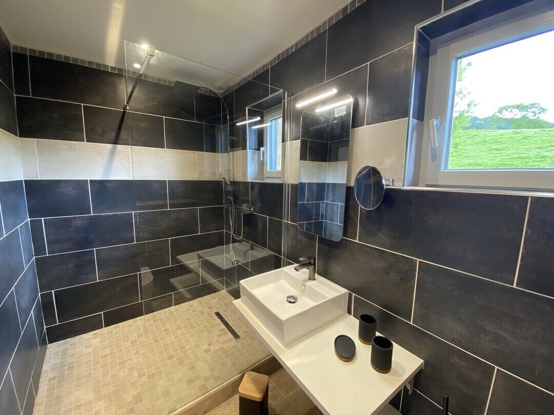 A modern bathroom with a large white sink, a mirror, and a window with a view of greenery.