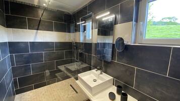 A modern bathroom with a large white sink, a mirror, and a window with a view of greenery.